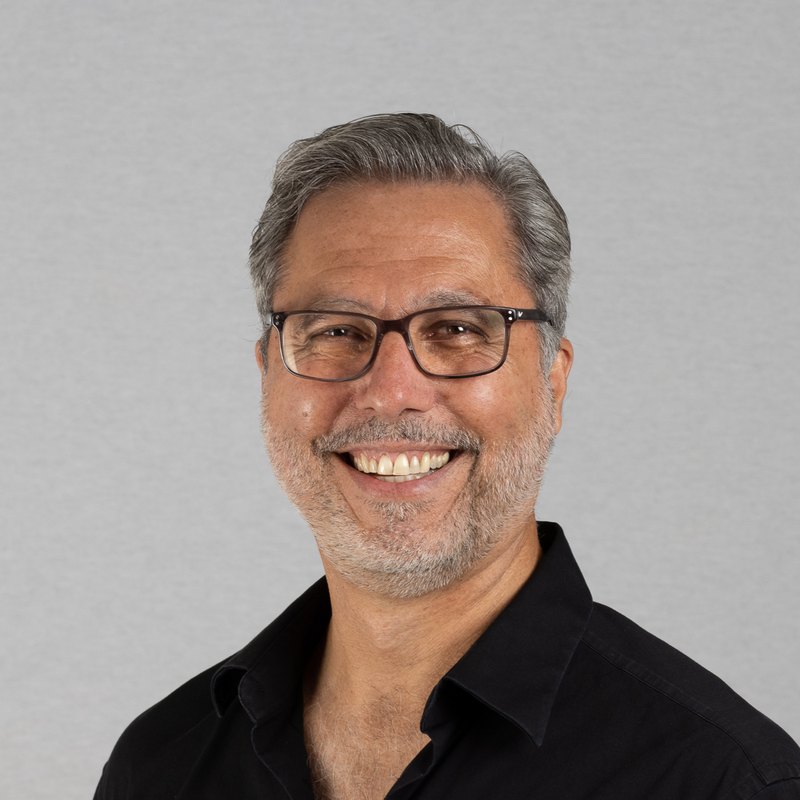 Actor headshot of a smiling man with grey hair and glasses in a black shirt
