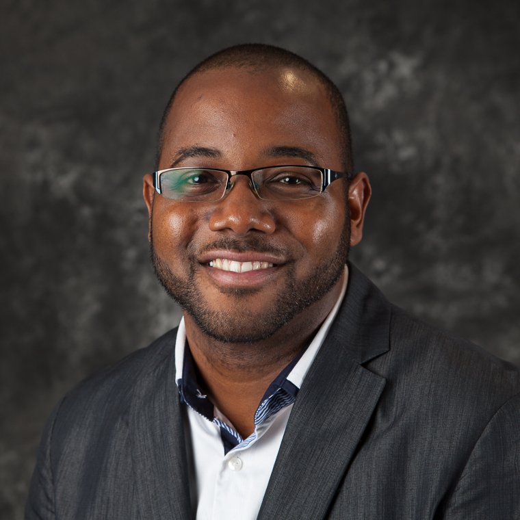 Corporate headshot of a smiling man in glasses and a gray blazer