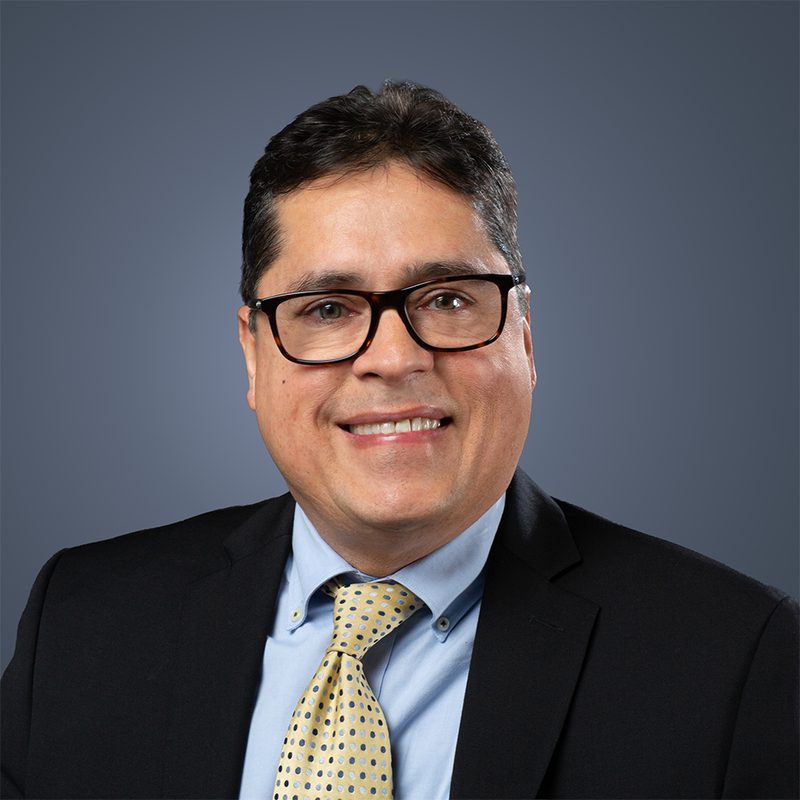 Finance professional headshot of a smiling man in a dark suit and yellow patterned tie