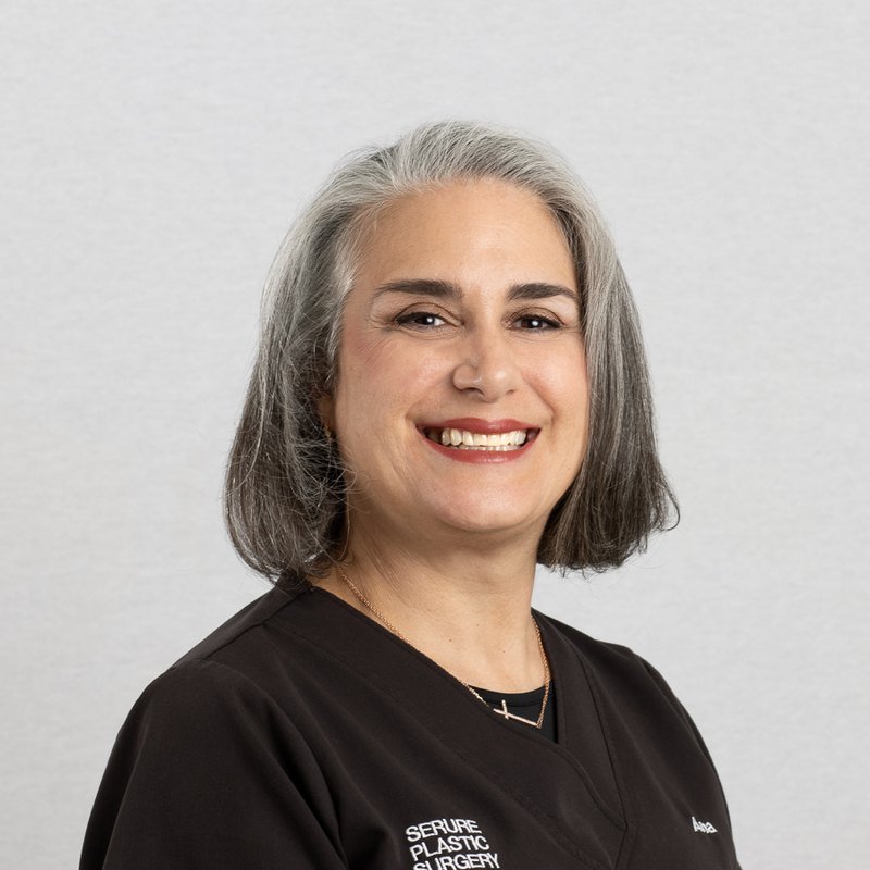 Medical headshot of a smiling clinician with grey hair in black scrubs