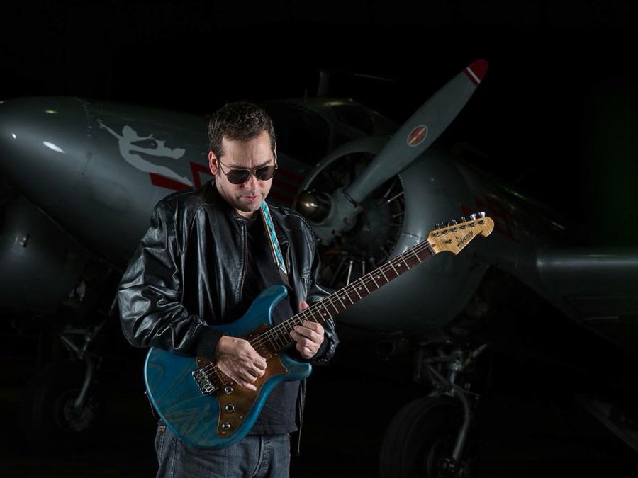 Guitarist photographed in a hangar in front of a vintage aircraft
