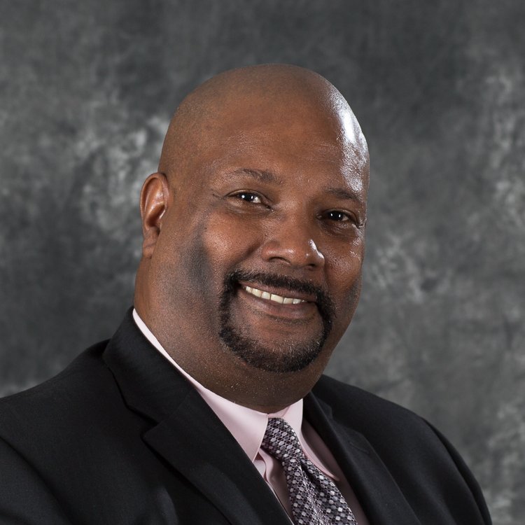 Professional headshot of a smiling man in a dark suit and tie