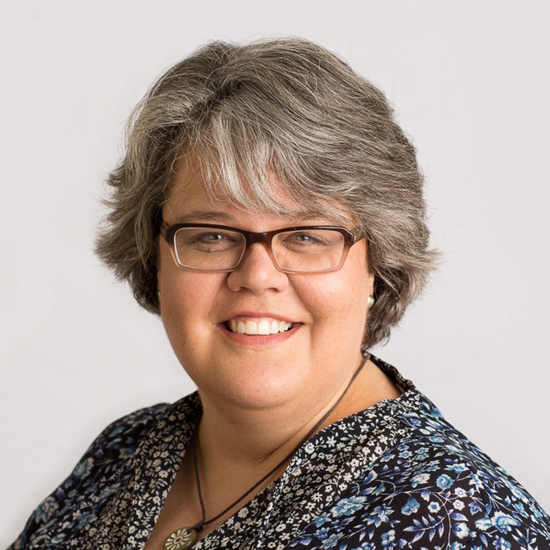 Real estate agent headshot of a smiling woman with glasses in a floral blouse