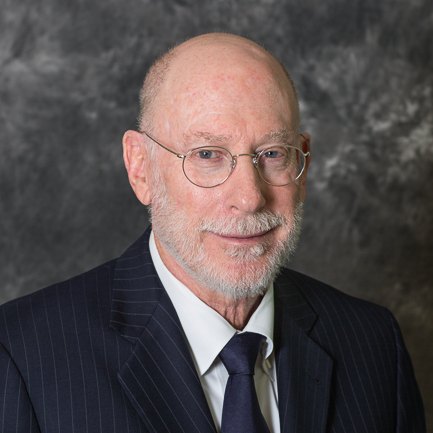 On-location headshot of a smiling man with glasses and a grey beard in a pinstripe suit